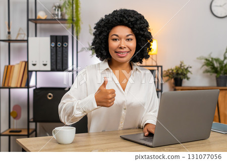 African American businesswoman gives thumbs up at laptop smiling approving successful result today African American businesswoman gives thumbs up at laptop smiling approving successful result today 131077056