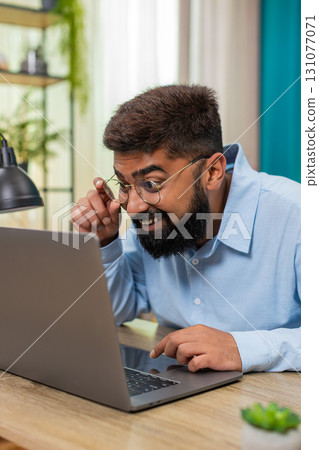 Indian man smiles after email reply on laptop nods celebrating project finish success indoors table Indian man smiles after email reply on laptop nods celebrating project finish success indoors table 131077071