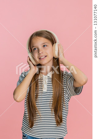 Child girl kid happily dances in wireless headphones enjoying favorite music smiling brightly 131077140