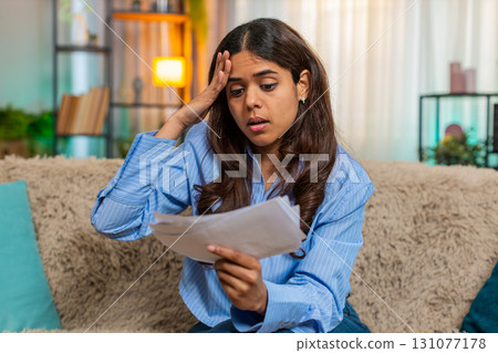 Indian woman in stress while looking at unpaid bills on home sofa with frustrated expression Indian woman in stress while looking at unpaid bills on home sofa with frustrated expression 131077178