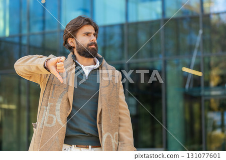 Upset young Indian man tourist showing thumb down expressing discontent on downtown city street Upset young Indian man tourist showing thumb down expressing discontent on downtown city street 131077601