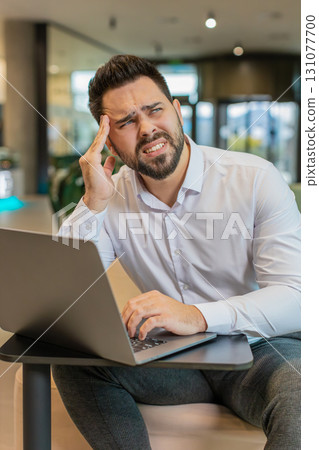 Tired ill young businessman using laptop suffering from headache problem tension in hotel lobby Tired ill young businessman using laptop suffering from headache problem tension in hotel lobby 131077700