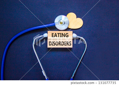 Eating disorders symbol. Concept words Eating disorders on beautiful wooden blocks. Wooden heart and stethoscope. Beautiful black background. Medical healthy lifestyle eating disorders concept. 131077735