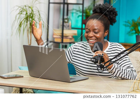 African American young woman blogger recording podcast smiling sitting on sofa using laptop at home African American young woman blogger recording podcast smiling sitting on sofa using laptop at home 131077762