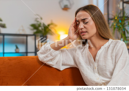Sick woman suffering from headache tension and migraine sitting on couch in living room at home Sick woman suffering from headache tension and migraine sitting on couch in living room at home 131078034