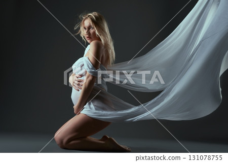 Pregnant woman in sagging fabric sitting on her knees 131078755