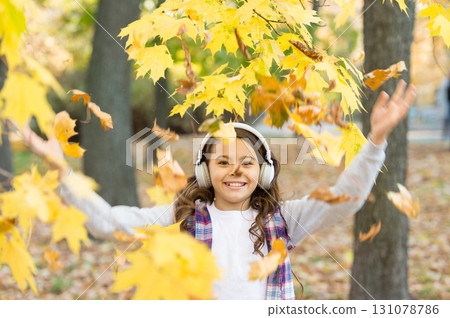 Melody of autumn. Schoolgirl listening modern headphones. Headphones technology. Falling leaves. Happy little girl wear headphones autumn nature background. Cute child smile with stereo headphones Melody of autumn. Schoolgirl listening modern headphones. Headphones technology. Falling leaves. Happy little girl wear headphones autumn nature background. Cute child smile with stereo headphones 131078786