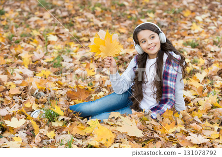 Thoughtful beauty. autumn kid fashion. inspiration. happy childhood. back to school. girl among maple leaves relax in park. fall in forest. enjoy music in earphones. education online and e-learning 131078792
