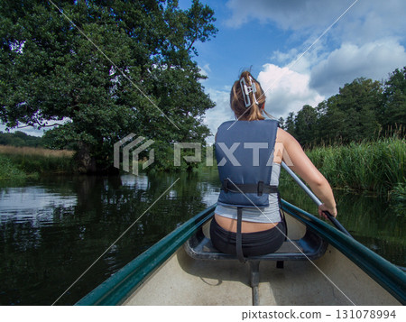 A young woman seen from behind canoeing in a river. Dark summer clouds in the background 131078994