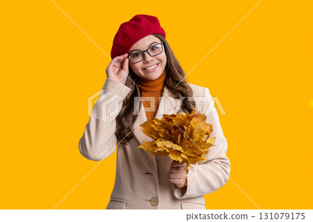 Fall leaves. Girl in fall style. Fall style fashion. Autumn leaves in hand teen girl. Autumn leaves and teen young girl isolated on yellow. Teenager girl in autumn beret and glasses 131079175