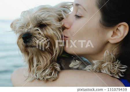 Tender portrait of young woman hugging and kissing small Yorkshire terrier dog. Emotional moment showing love, care, friendship and human animal bond. 131079439