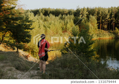 A person strolls along a sandy trail in the woods with a dog on a sunny day. A mature woman with a towel walks along a sandy path towards green forest 131079444