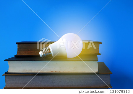 Light bulb and hard cover books on background. 131079513