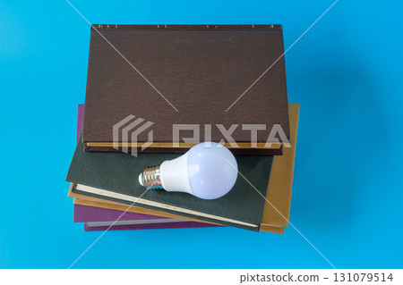 Light bulb and hard cover books on background. 131079514