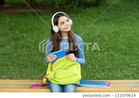 Education and knowledge. Girl listening to audiobook with book. Audiobook. School education. Student life. School girl listen audiobook in headphones outdoor. Back to school. Look for inspiration Education and knowledge. Girl listening to audiobook with book. Audiobook. School education. Student life. School girl listen audiobook in headphones outdoor. Back to school. Look for inspiration 131079614
