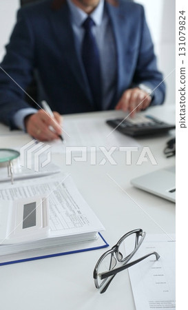 Close up of calculator while male accountant calculating taxes and analyzing financial data in office setting. Audit and taxes in business Close up of calculator while male accountant calculating taxes and analyzing financial data in office setting. Audit and taxes in business 131079824