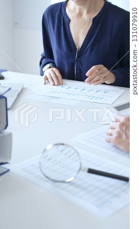 Female accountant reviewing financial documents, working collaboratively at white desk with blue folder stack, highlighting teamwork and business productivity. Audit and taxes in business Female accountant reviewing financial documents, working collaboratively at white desk with blue folder stack, highlighting teamwork and business productivity. Audit and taxes in business 131079910