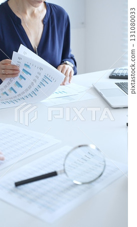 Female accountant reviewing financial documents, working collaboratively at white desk with blue folder stack, highlighting teamwork and business productivity. Audit and taxes in business Female accountant reviewing financial documents, working collaboratively at white desk with blue folder stack, highlighting teamwork and business productivity. Audit and taxes in business 131080033