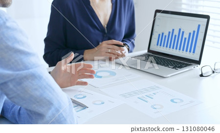 Business professionals collaborating on a laptop, reviewing financial documents, and discussing project strategies in a modern office. Businesspeople in finance concept 131080046