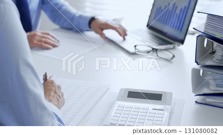 Two professional accountants analyzing financial documents and using a calculator with a laptop in a bright office. Audit and taxes in business 131080082
