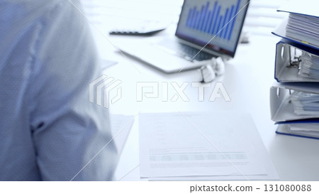 Corporate professionals reviewing financial documents, working collaboratively at white desk with blue folder stack, highlighting teamwork and business productivity. Audit and taxes in business Corporate professionals reviewing financial documents, working collaboratively at white desk with blue folder stack, highlighting teamwork and business productivity. Audit and taxes in business 131080088