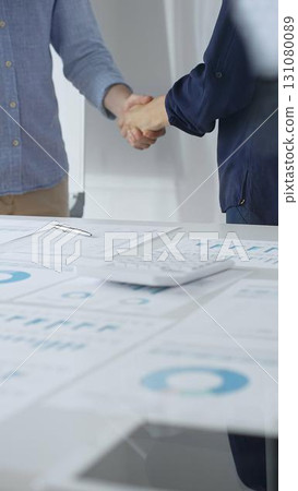 Business partners shaking hands after successful agreement over financial documents, calculator and pen on white table in office. Handshake concept Business partners shaking hands after successful agreement over financial documents, calculator and pen on white table in office. Handshake concept 131080089
