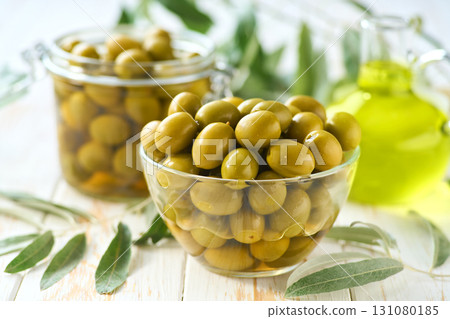 pickled green olives in a transparent glass bowl on a white wooden table, selective focus. 131080185