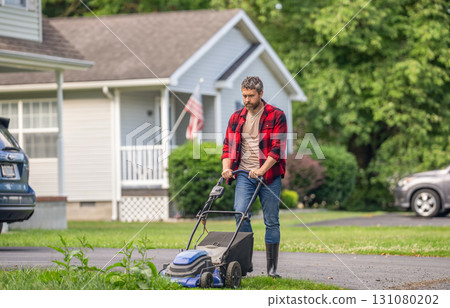 Hispanic gardener. Lawnmower mow green grass. Man gardener cut grass. Garden care. Electric lawn mower. Landscape design. Lawn mower landscaping. Backyard grass maintenance. Riding mower convenience 131080202