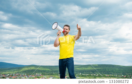 man in yellow shirt shout in loudspeaker on sky background. novelty 131080272