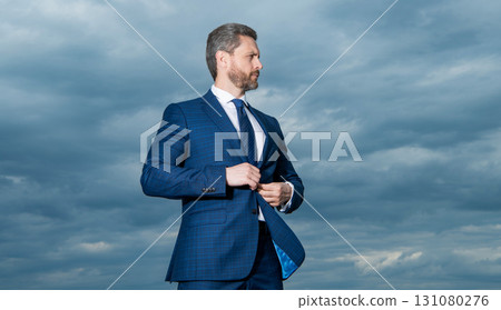 Professional man sky background. Grizzled man buttoning suit. Serious man looking aside outdoors Professional man sky background. Grizzled man buttoning suit. Serious man looking aside outdoors 131080276