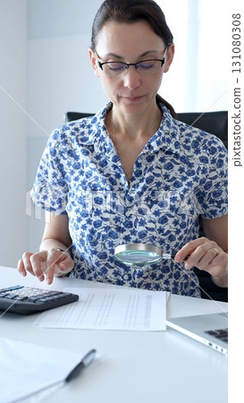 Professional female accountant examining financial documents with magnifying glass, focusing on meticulous verification of accounting records and audit details. Audit and taxes in business Professional female accountant examining financial documents with magnifying glass, focusing on meticulous verification of accounting records and audit details. Audit and taxes in business 131080308