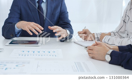 Business team collaborating in an office, analyzing financial data through digital tablets and documents during a meeting. Close up view of hands engaged in discussion and strategy planning 131080364