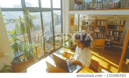 Woman working on laptop in sunlit modern apartment with plants a 131080383