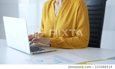 Unknown businesswoman wearing yellow blouse working on laptop at minimalist white desk in contemporary workplace, typing with focus. Business people concept Unknown businesswoman wearing yellow blouse working on laptop at minimalist white desk in contemporary workplace, typing with focus. Business people concept 131080514