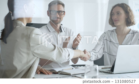 Businesswomen partners are shaking hands after successful negotiation, colleagues clapping, celebrating agreement in modern office headset. Handshake concept, view through the glass door Businesswomen partners are shaking hands after successful negotiation, colleagues clapping, celebrating agreement in modern office headset. Handshake concept, view through the glass door 131080527