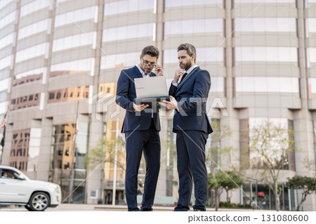 Business online. Men working on laptop. Businessmen working online. Businessmen in suit with laptop. Online working. Businessmen checking email. Business men freelancing outdoor. Business district Business online. Men working on laptop. Businessmen working online. Businessmen in suit with laptop. Online working. Businessmen checking email. Business men freelancing outdoor. Business district 131080600