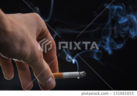 Steaming cigarette with smoke stream in male hand dark background, smoking 131081055