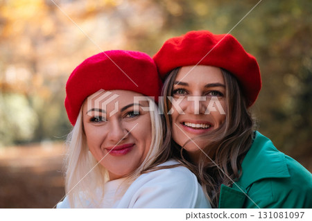 Berets Women Autumn Portrait: Two smiling women wearing red berets pose outdoors during autumn. 131081097
