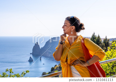 Woman, ocean, cliff overlooking scenic coastal landscape with rock formations and bright blue sky, ideal copy space 131081113
