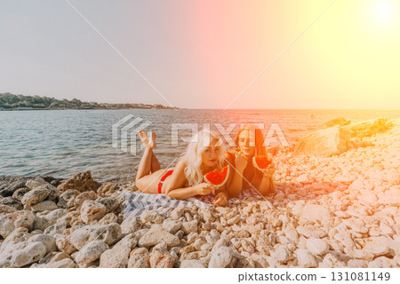 Beach Women Watermelon: Summer fun, two women enjoy watermelon on rocky beach, sunny day. 131081149