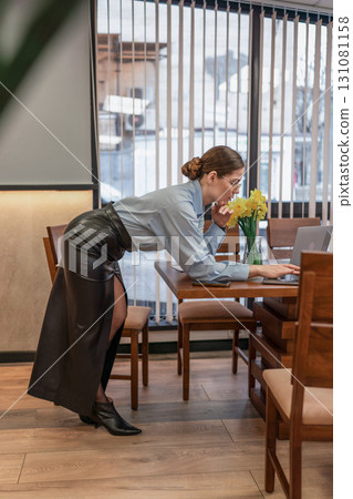 Woman Laptop LeatherSkirt: Lady works at table on laptop in cafe near window during day. Woman Laptop LeatherSkirt: Lady works at table on laptop in cafe near window during day. 131081158