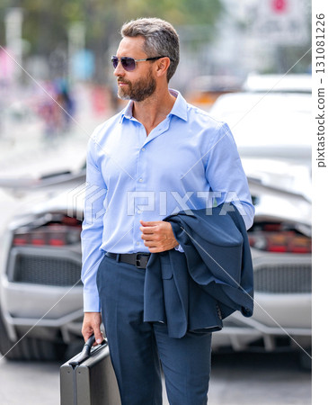 Corporate business. Luxury businessman in suit. Business leader portrait. Successful businessman walking with briefcase at parking. Businessman hold briefcase. Mature businessman in suit Corporate business. Luxury businessman in suit. Business leader portrait. Successful businessman walking with briefcase at parking. Businessman hold briefcase. Mature businessman in suit 131081226