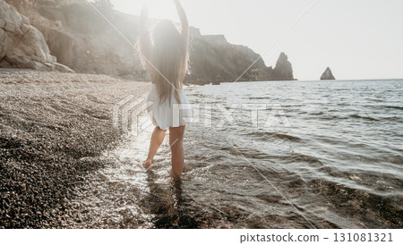 Woman in White Dress Walks on a Beach at Sunset 131081321