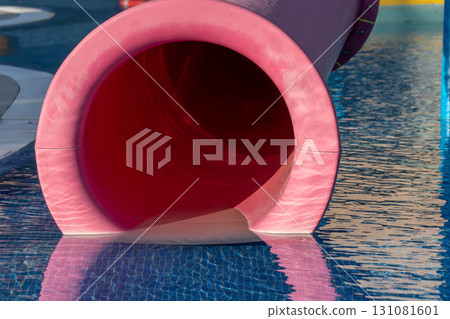 Water Slide Pool Fun Pink Entrance Close-up. A close-up view of a pink waterslide's opening, revealing a dark blue pool beneath. The slide appears to be wet, suggesting recent use. 131081601