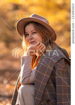 Woman Autumn Hat Portrait: Smiling woman wearing hat sits outdoors in autumnal setting, capturing fall fashion and mood. Woman Autumn Hat Portrait: Smiling woman wearing hat sits outdoors in autumnal setting, capturing fall fashion and mood. 131081623