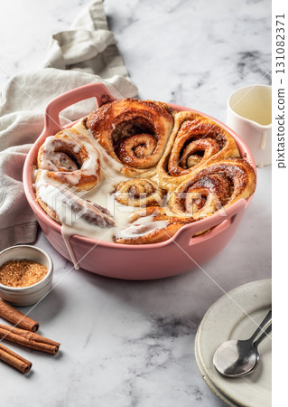 Freshly baked glazed cinnabon buns in a ceramic baking dish on white marble background. Making cinnamon rolls process Freshly baked glazed cinnabon buns in a ceramic baking dish on white marble background. Making cinnamon rolls process 131082371