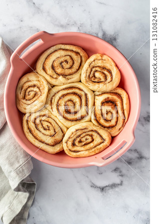Raw cinnabon buns in a ceramic baking dish on white marble background top view. Making cinnamon rolls process. Cinnabon preparation Raw cinnabon buns in a ceramic baking dish on white marble background top view. Making cinnamon rolls process. Cinnabon preparation 131082416