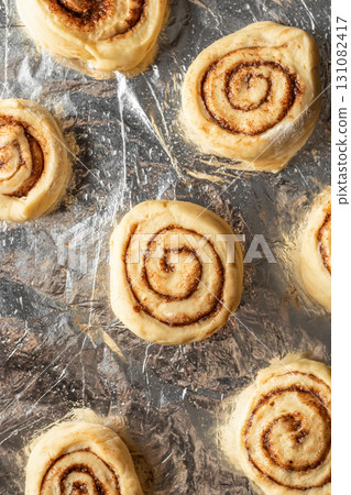 Raw cinnabon buns on a baking sheet top view. Making cinnamon rolls process. Cinnabon preparation Raw cinnabon buns on a baking sheet top view. Making cinnamon rolls process. Cinnabon preparation 131082417