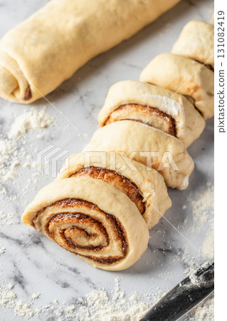 Cutted roll of dough on white marble background. Making cinnamon rolls process. Cinnabon preparation 131082419
