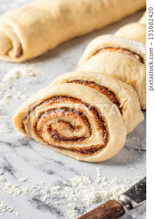 Cutted roll of dough on white marble background. Making cinnamon rolls process. Cinnabon preparation 131082420